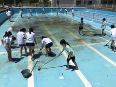 水を抜いたプールの中を複数の児童達がデッキブラシで磨いている写真