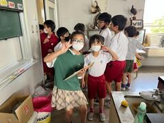 2人の女子児童がピースをしており、その後ろに複数の児童達が立っている写真