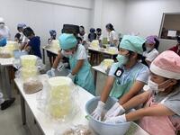 エプロンと三角巾を被った児童達が手袋をして、ボウルのようなものの中で味噌を作っている写真