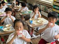 教室のような所で椅子に座った児童達が紙パックの牛乳を飲んでいる写真
