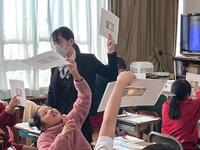 制服を着た女性や複数の児童達がお札1枚と紙を合わせ透けている様子を見ている写真