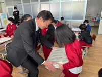 教室で男性が児童に一億円分の重しを持たせている写真