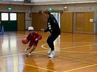 帽子を被った児童がボールをドリブルしながら男性にとられないようにしている写真