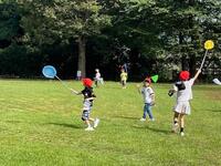 周りが木々で囲まれた公園内で児童達が虫取り網を手に持っている写真
