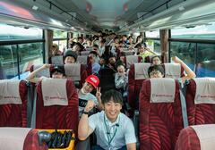 先生を先頭に、児童達がバスの中で座りながらポーズをとっている写真