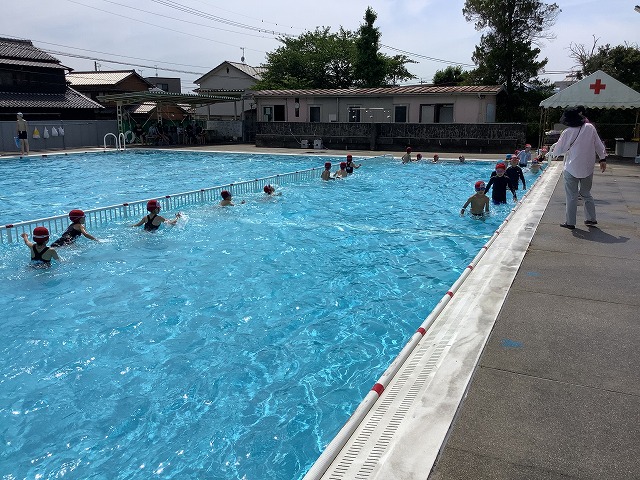学校のプールで列になって水中歩行を行う児童達の写真