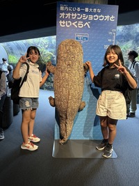 京都水族館で模型のオオサンショウウオを挟み、記念撮影をしている生徒2人の写真