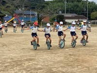 5人の生徒が手をつなぎ、横一列に一輪車をこいでいる写真