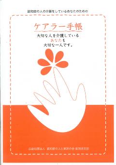 橙色の文字で「ケアラー手帳表紙」と書かれその下に白と橙の二色で描かれた手のイラスト