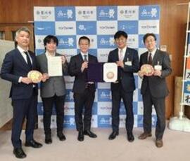 スーツ姿の男性5名がそれぞれ協定書か豊川市高齢者みまもり隊ワッペンを両手に持って横に並んで立っている写真