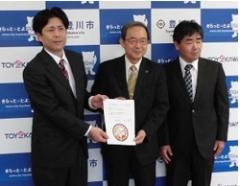 スーツ姿の男性3人が横に並んで立ち、うち2名が協定書を前に見せるようにして、手に持っている様子の写真
