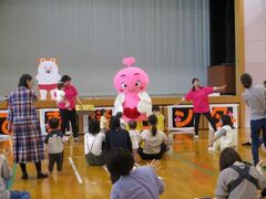 ピンク色のキャラクターの着ぐるみを着た人と左右で手を広げている濃いピンクの服を着た女性の写真