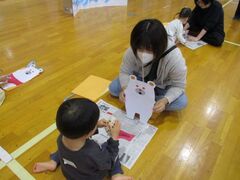 シロクマのイラストを立たせて持っている女性とその正面で何かを作っている子供の写真