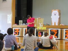体育館にて親子が絵本の読み聞かせを聞いている写真