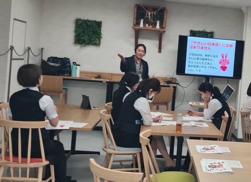 スーツを着た女性が、座っている銀行員の女性たちの前で説明している写真