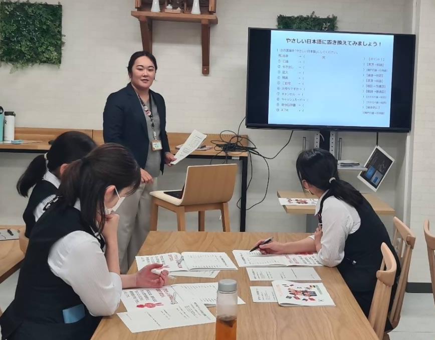 3人の銀行員の女性が練習問題に取り組み、スーツを着た女性と答え合わせしている写真