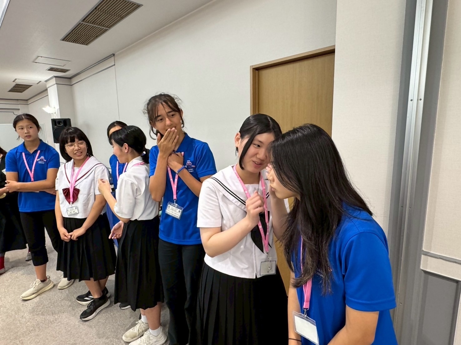 青い服を着た人制服を着ている人が伝言ゲームをしている写真