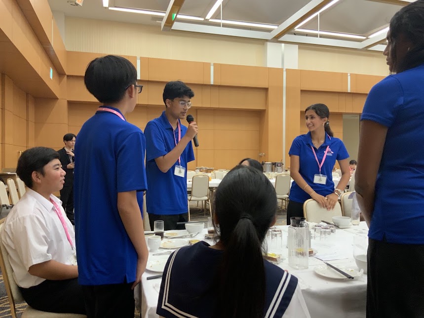 青い服を着た人がマイクで話をしている様子