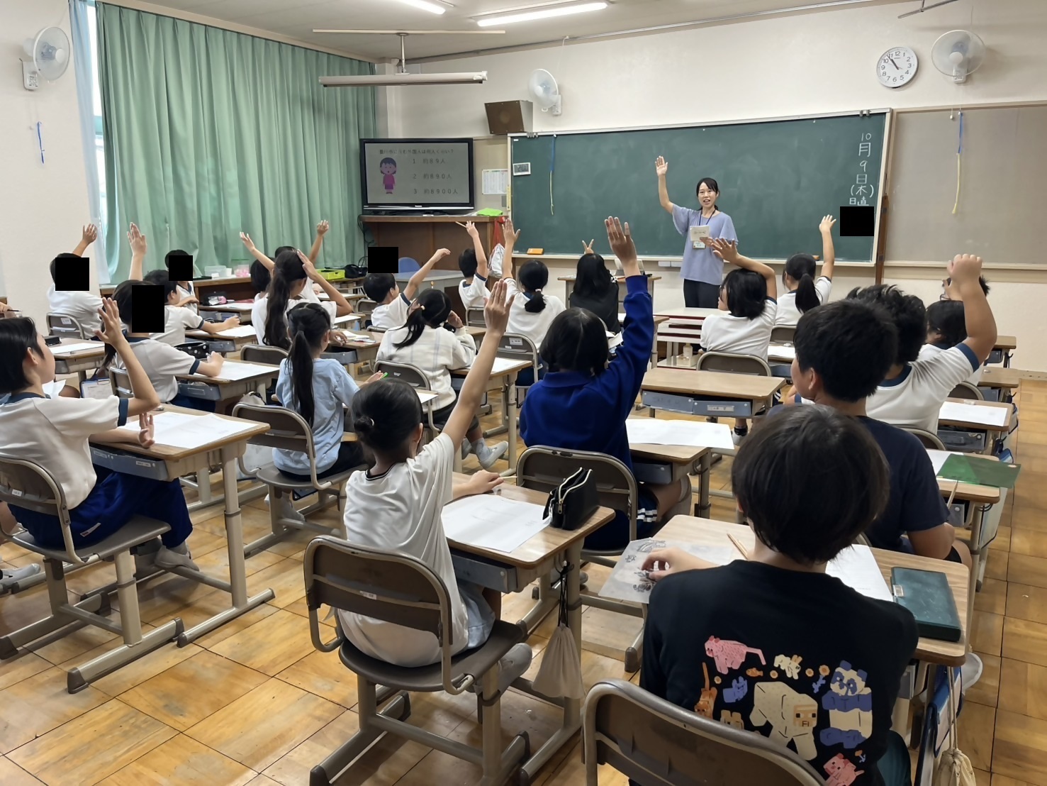 教室で子どもたちが手を挙げて発言しようとしている写真