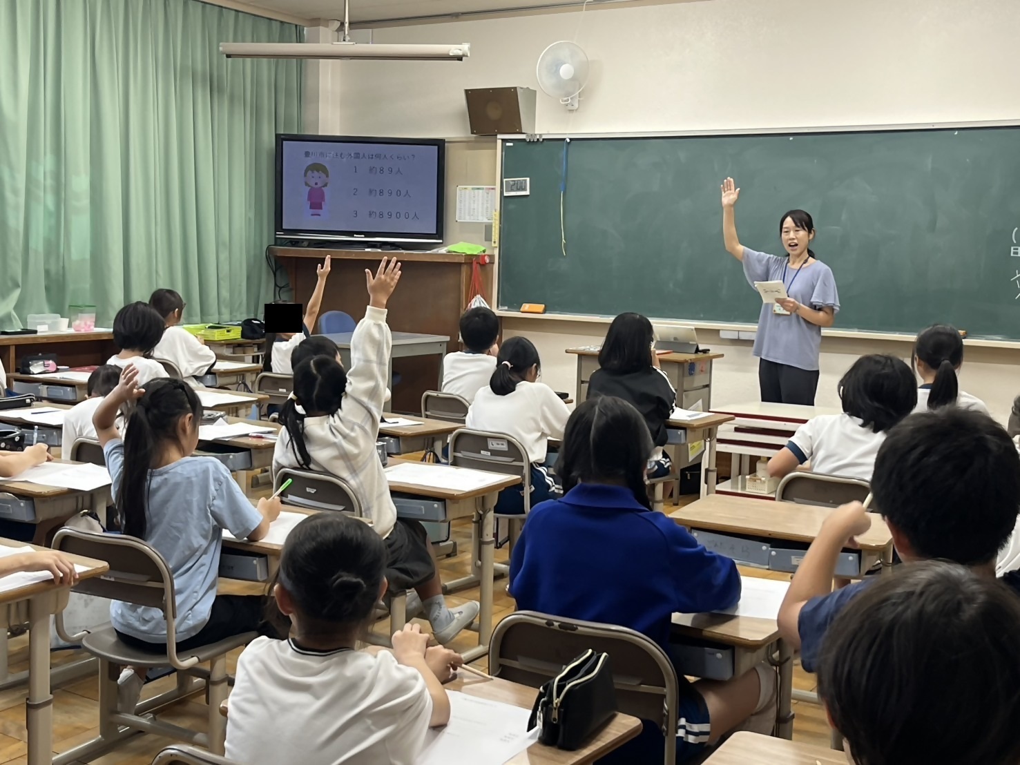 教室で子どもたちが手を挙げて発言しようとしている写真