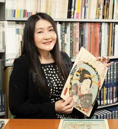黒髪の女性が浮世絵を持って笑っている写真