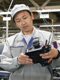 作業着を着た男性が黒い部品を両手で持ち上げて確認している写真