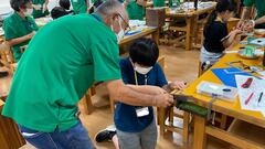 テーブルの端でパーツを切るためにのこぎりを使う少年の写真