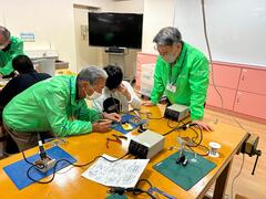 講師の人たちに教えられながらはんだごてで接着作業をする写真