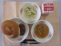 テーブルクロスに並べられたサンドイッチバンズパン・牛乳・コンソメスープ・てりやきハンバーガー(てりやきハンバーグ/キャベツソテー)の写真