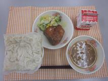 テーブルクロスに並べられた白玉うどん・牛乳・カレーなんばん・ぶりの竜田揚げ・コーンサラダの写真