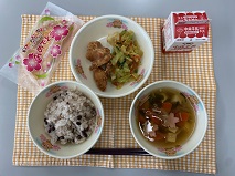 テーブルクロスに並べられた赤はん・牛乳・すまし汁・とりのから揚げ・ごまあえ・米粉のいちごクレープの写真