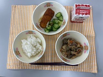 テーブルクロスに並べられたごはん・牛乳・煮しめ・いかフライのレモン煮・きゅうりあえの写真