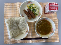 テーブルクロスに並べられた白玉うどん・牛乳・カレーなんばん・ちくわの青じそ揚げ・コーンサラダ・コーンドレッシングの写真