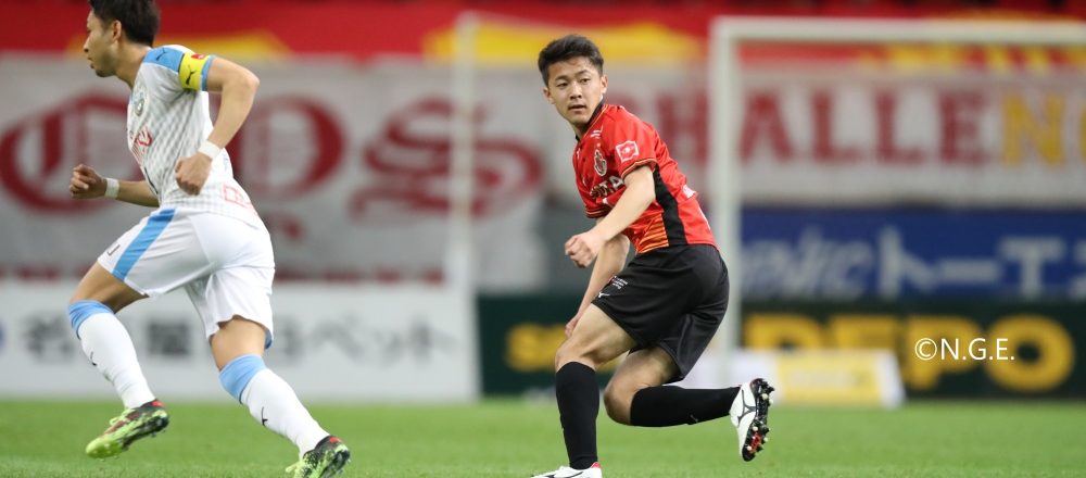 サッカー場のような所でユニフォームを着用した男性が試合を行っている写真