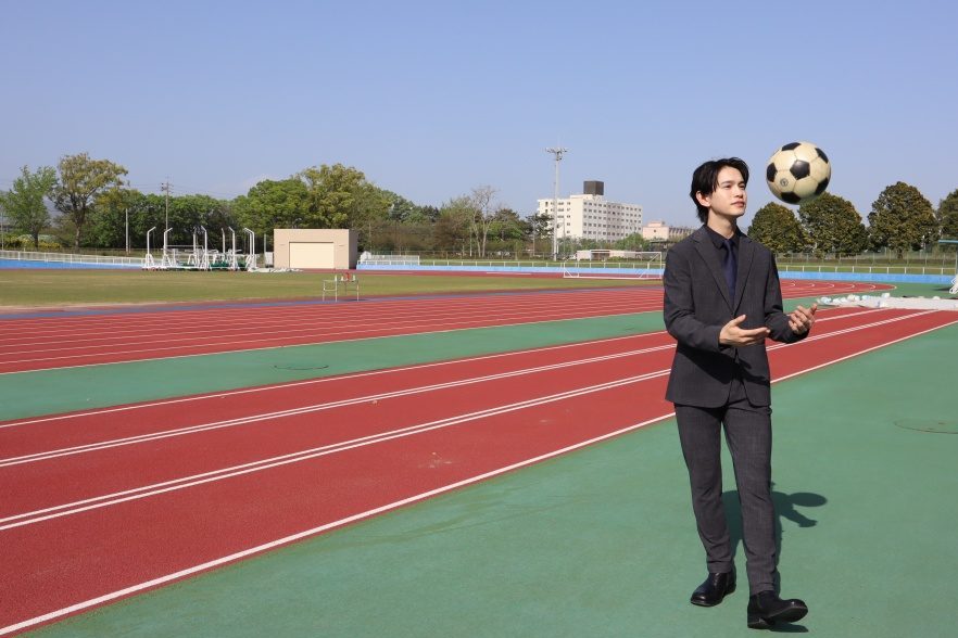 競技場でスーツを着た男性が手を使ってサッカーボールを上げている写真