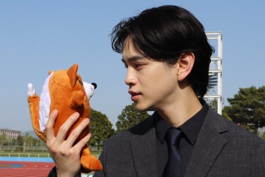 狐をイメージした豊川市の公式キャラクター「いなりん」のぬいぐるみを手に持ち見ている男性の写真