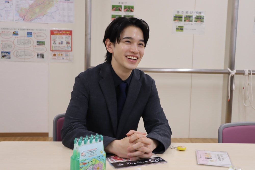 テーブルの上に手を組みながら椅子に座り笑顔で話をしている男性の写真