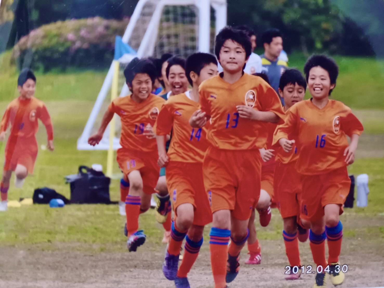 芝生の上でユニフォームを着た複数の子供達がランニングを行っている写真