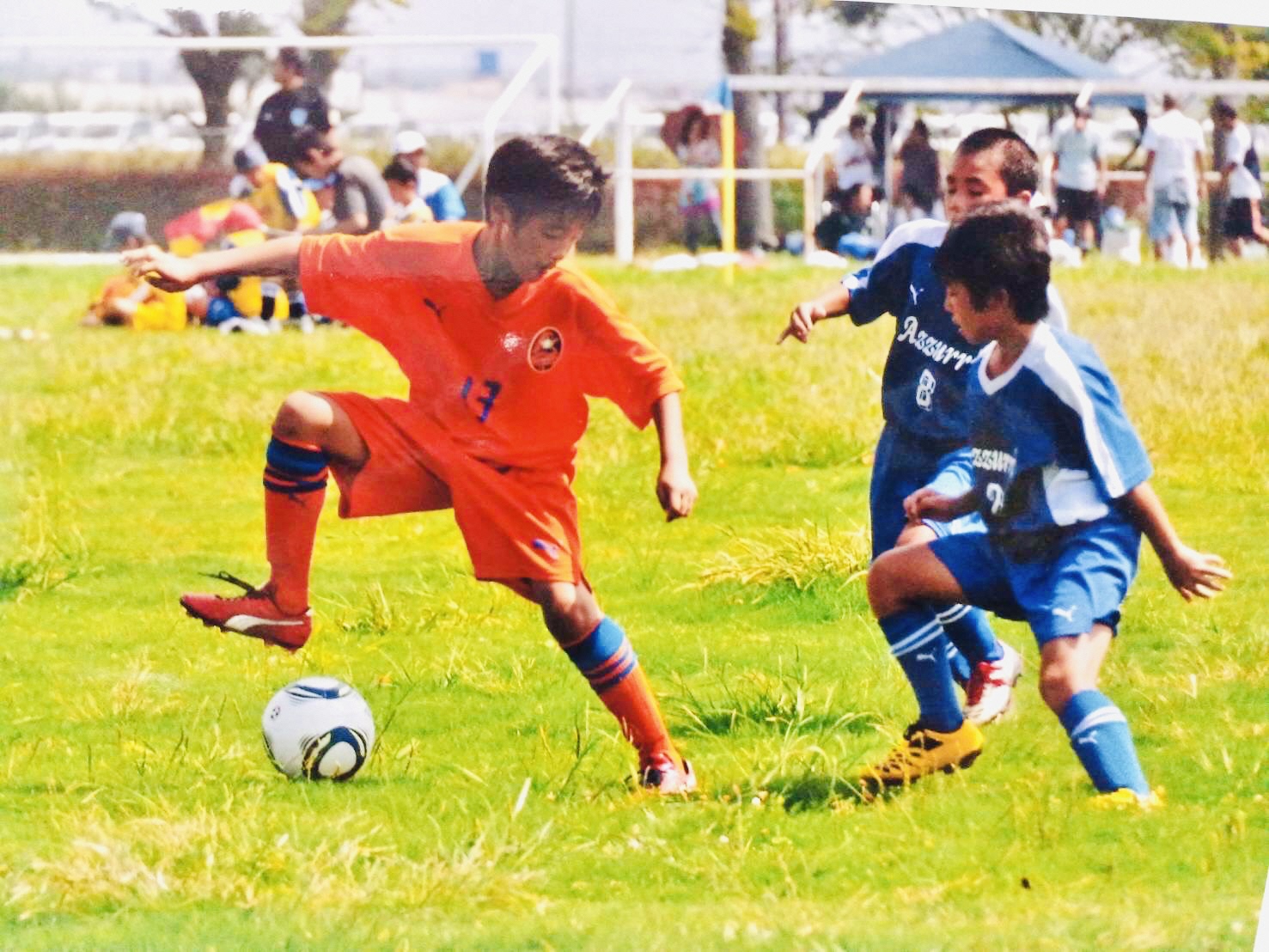 ユニフォームを着用した3人の子供がサッカーを行っている写真