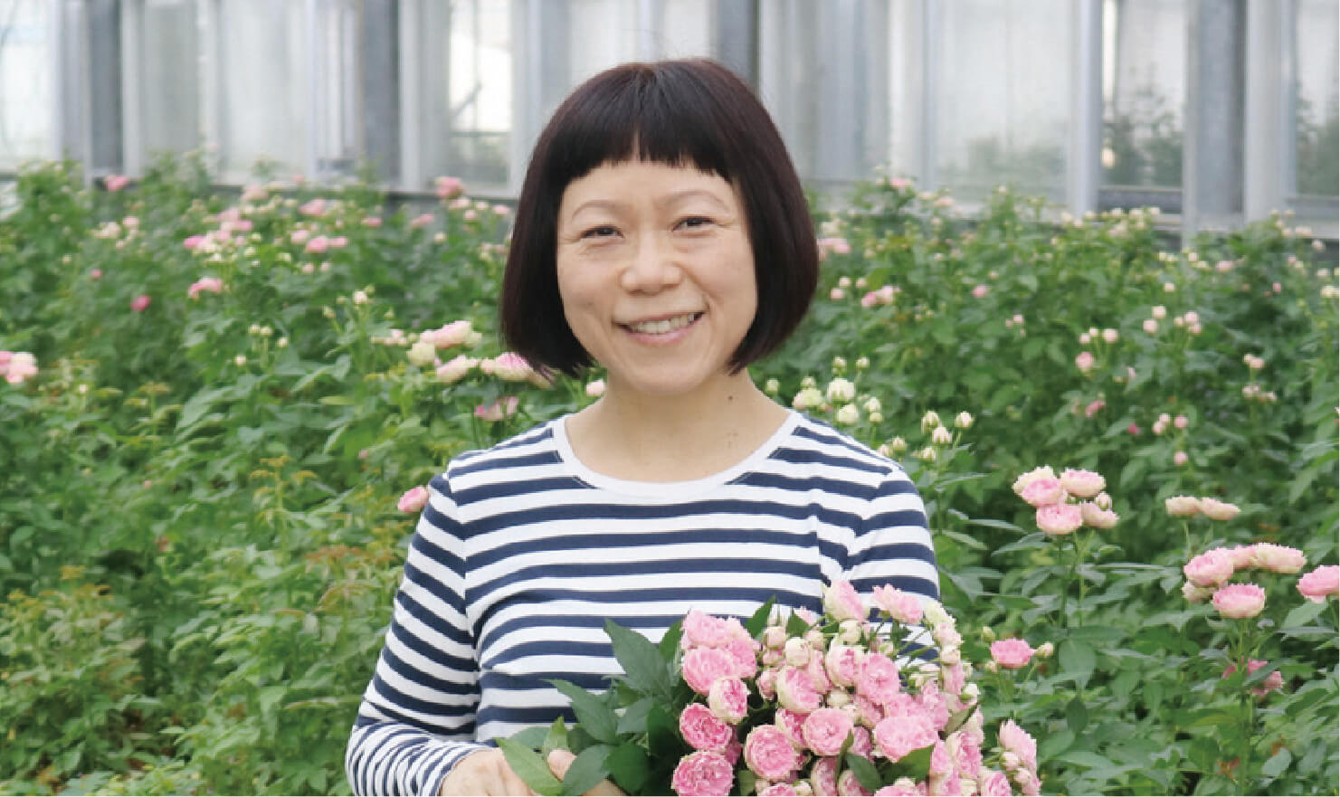 お花を持った女性がお花畑の前で笑顔で微笑んでいる写真
