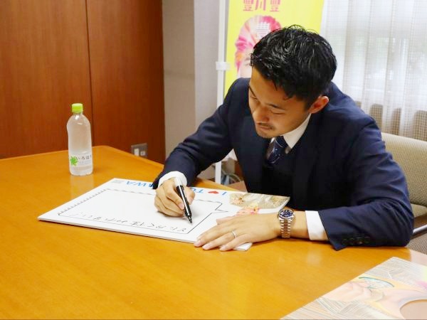 スーツを着た男性がペンを持ち、ボードのようなものに文字を書いている写真