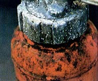 赤い消火器の上部が、あばた状にところどころ黒く腐食している写真