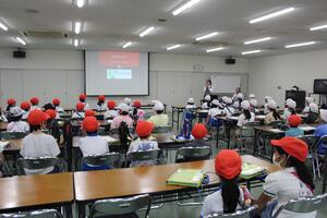 広い部屋で児童が座りスクリーンの映像を見ている写真