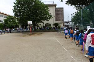 児童が列を作って、小学校の校庭にある水溜まりをよけて歩いている写真