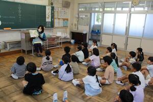 児童たちが間隔をあけて体育座りをして読み聞かせに耳を傾けている写真