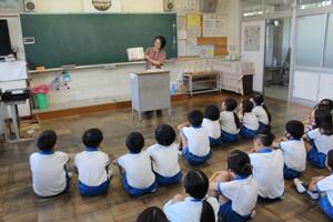 体操着を着た児童たちが体育座りをして読み聞かせを聞いている写真