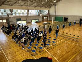 児童たちが列になって体育館へ入場し並べられた椅子に着席している写真