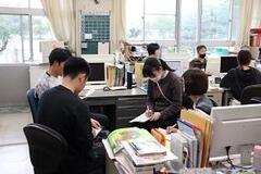 職員室内で寄せ合った椅子に座り、会話やメモ取りを行う教師達の写真