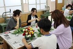 室内の新聞紙が敷かれた机の上で花を束ねる作業をしている人々の写真