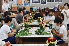 室内の机の上に新聞紙が敷かれており、その上で花を束ねたりしている人々の写真